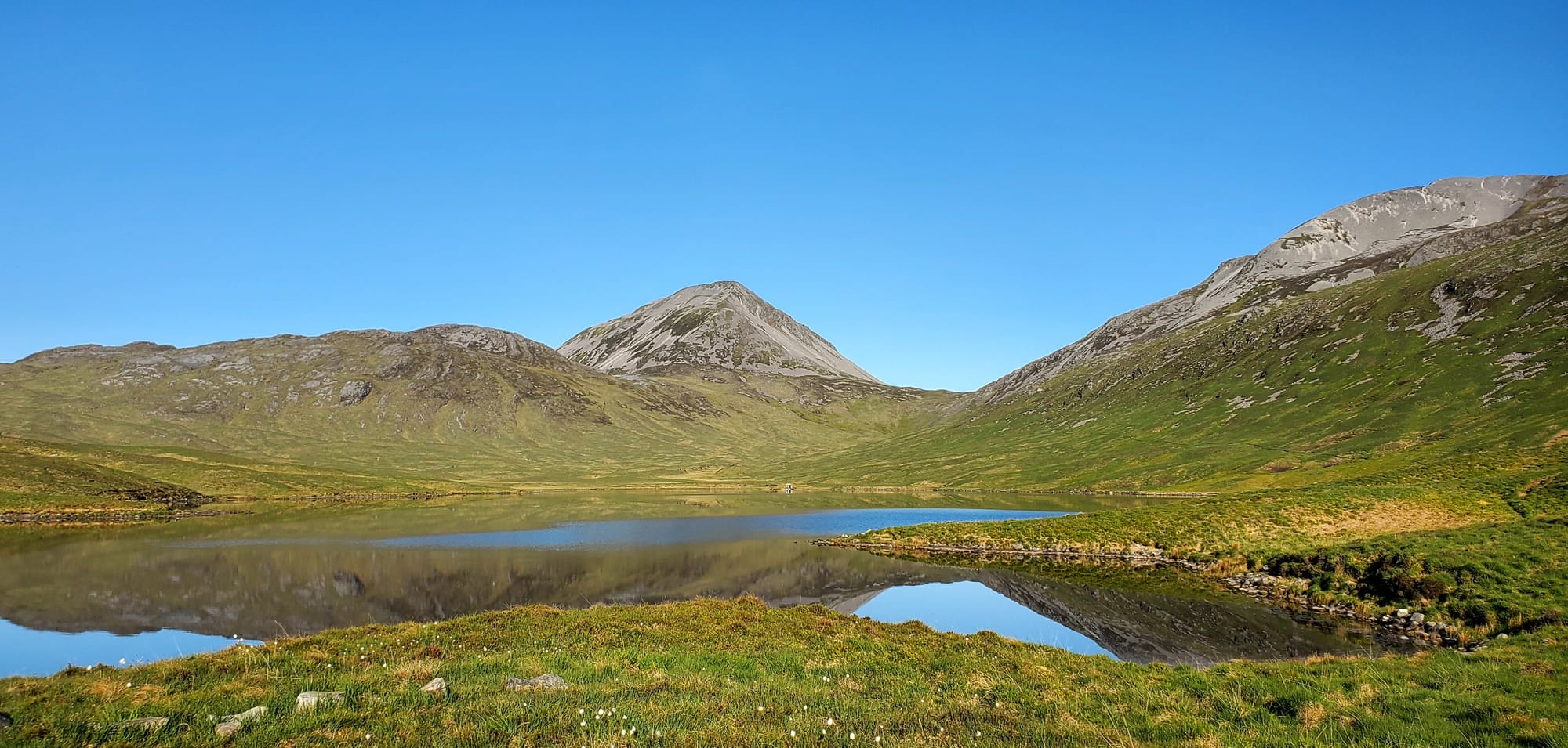 Loch an t-Siob reflecting the hills behind it on a sunny day with a blue sky.