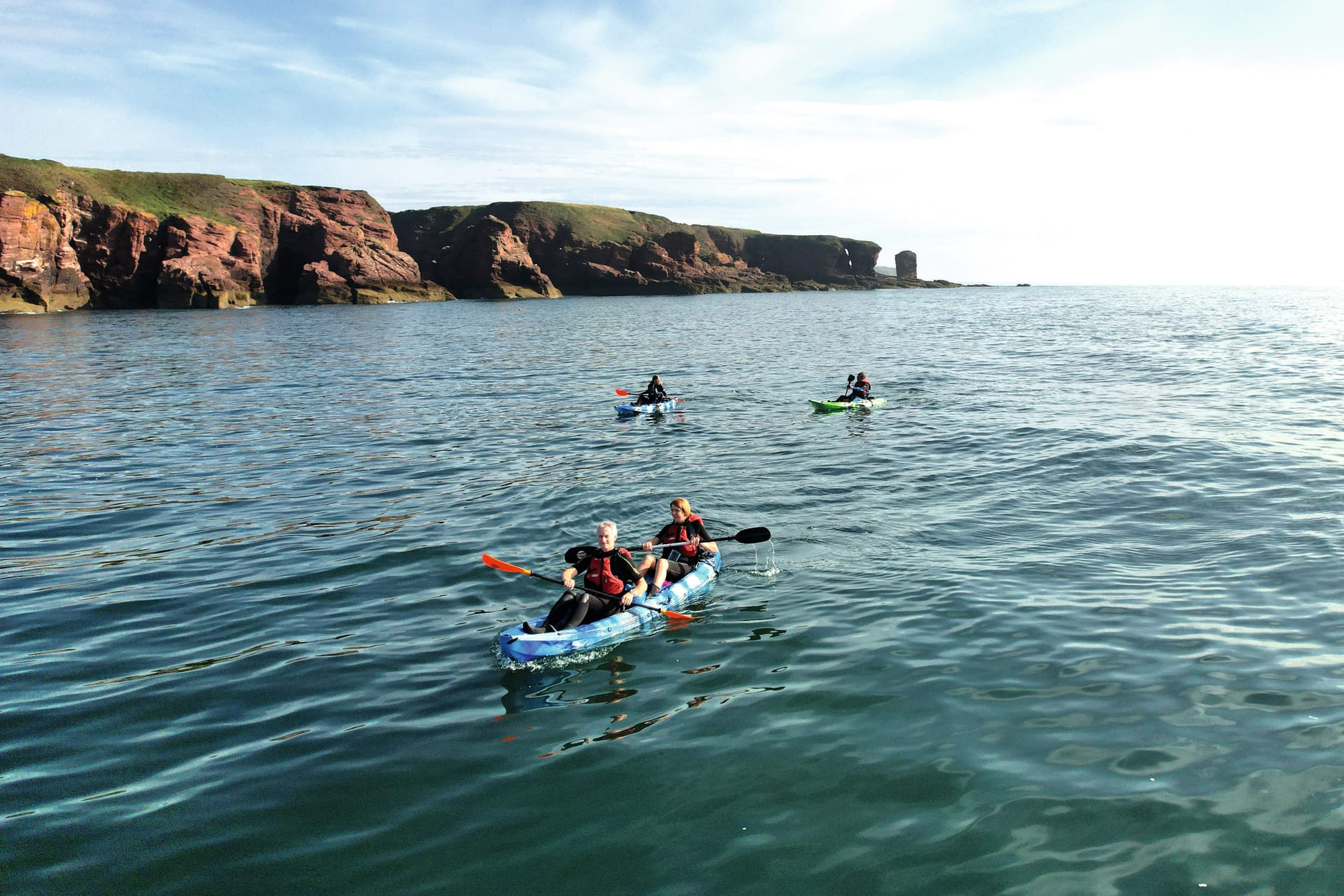 A group of kayaks travelling parallel to the red cliffs. 
