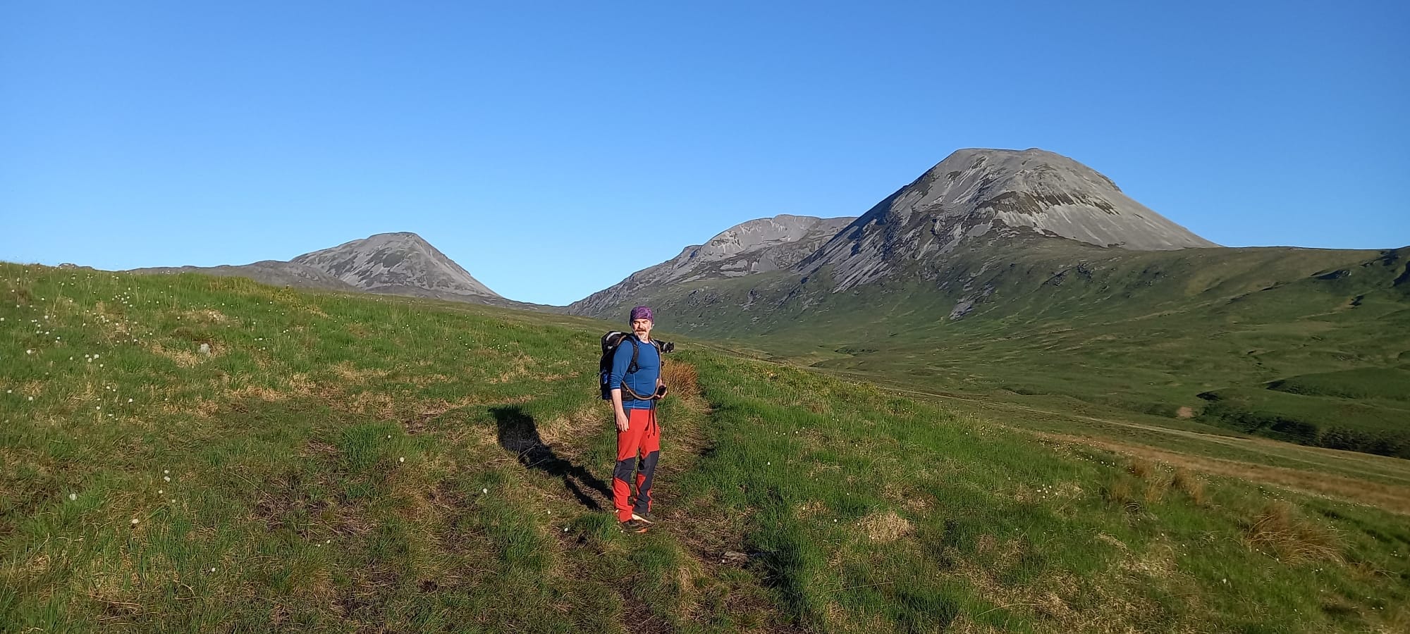 Robert is wearing hiking gear standing on green grass with the Paps of Jura in the background.