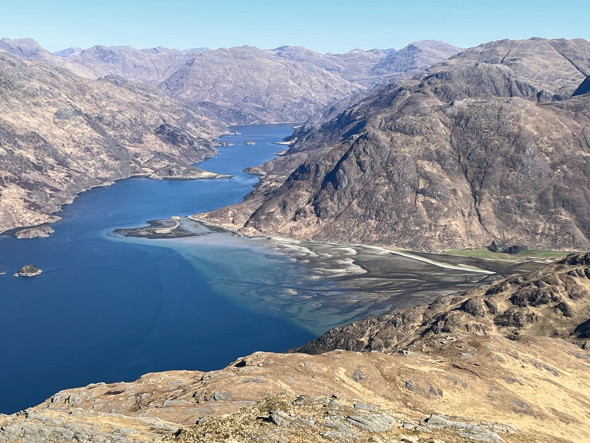 Looking down over brown mountains from the summit of Ladhar Bheinn. The water is blue and there are sections of sediment in the bays.
