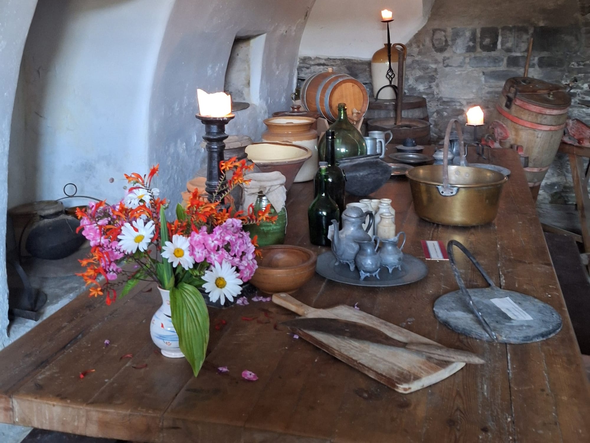 A large wooden table is covered with ephemera, including candles, pots and flowers. 