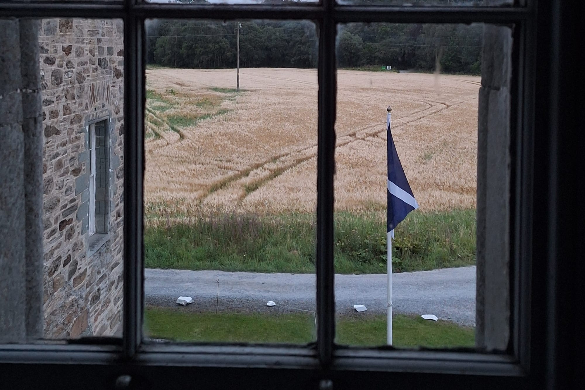 Looking out the castle window to see a Saltire on a flagpole next to a field. 