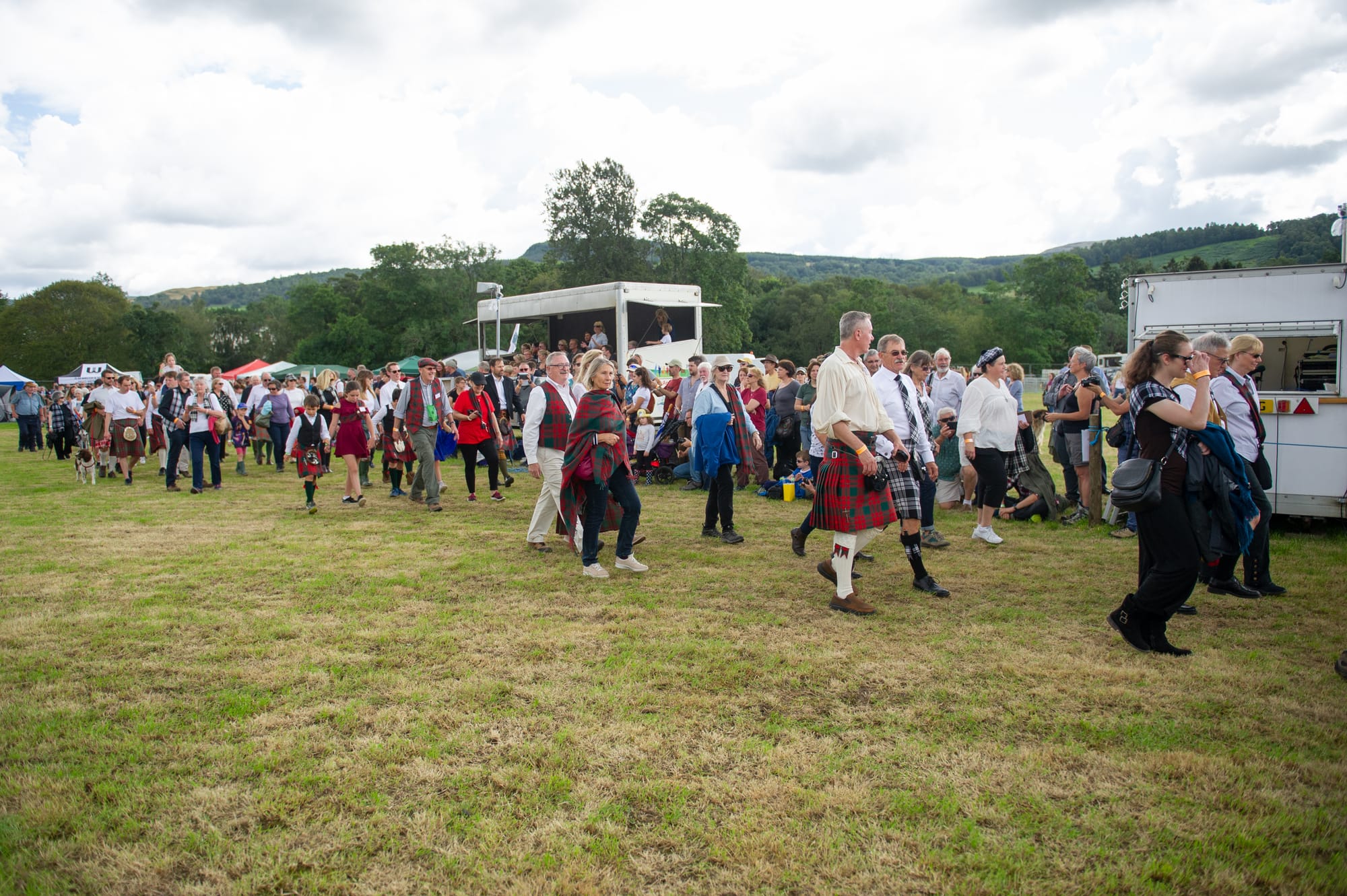 Clan Menzies marching on green grass. People are wearing tartan and highland dress. 