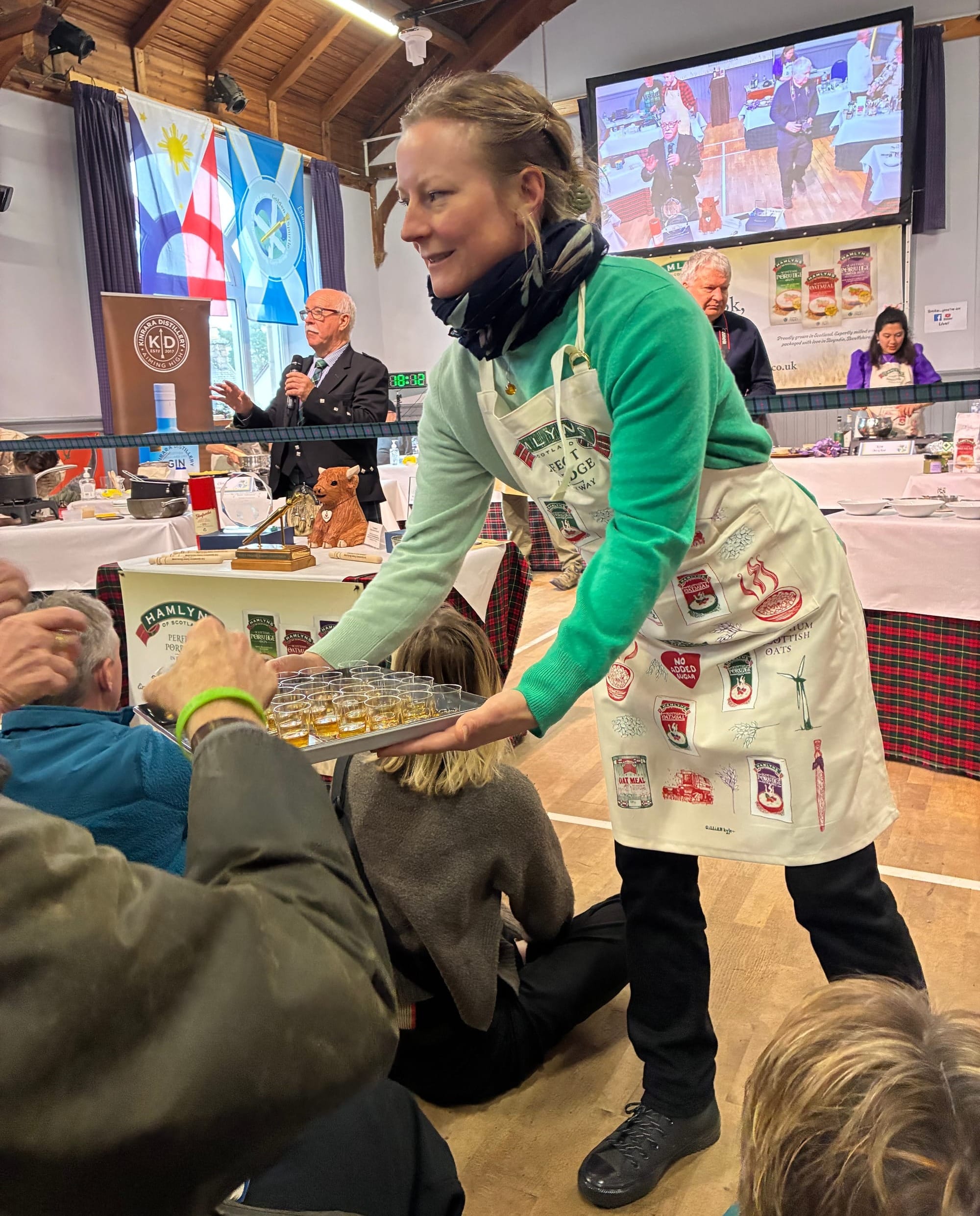 A woman passes out a tray of small shot glasses of whisky to the audience.