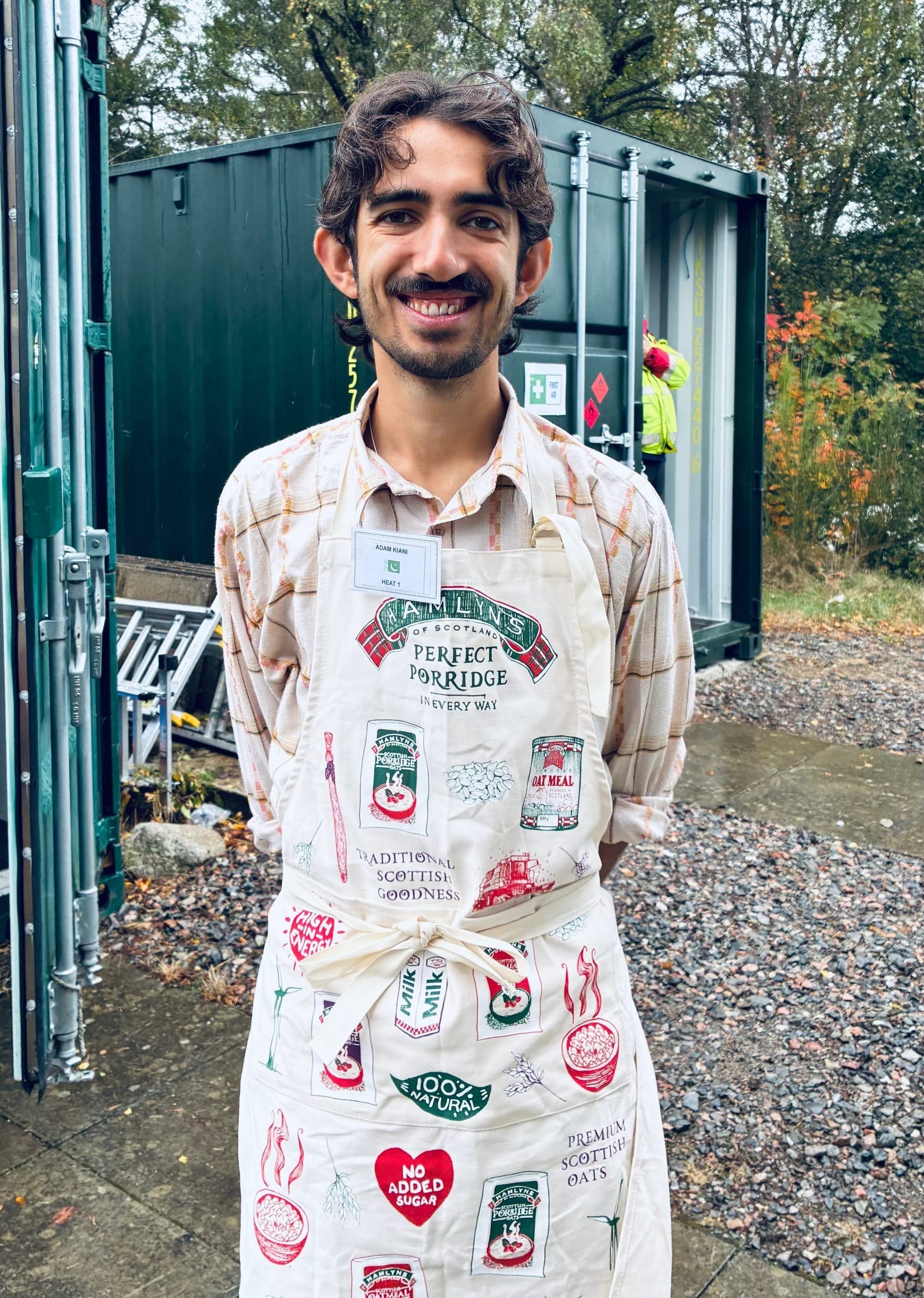 Adam Kiani smiles, wearing an apron with porridge illustrations on it.