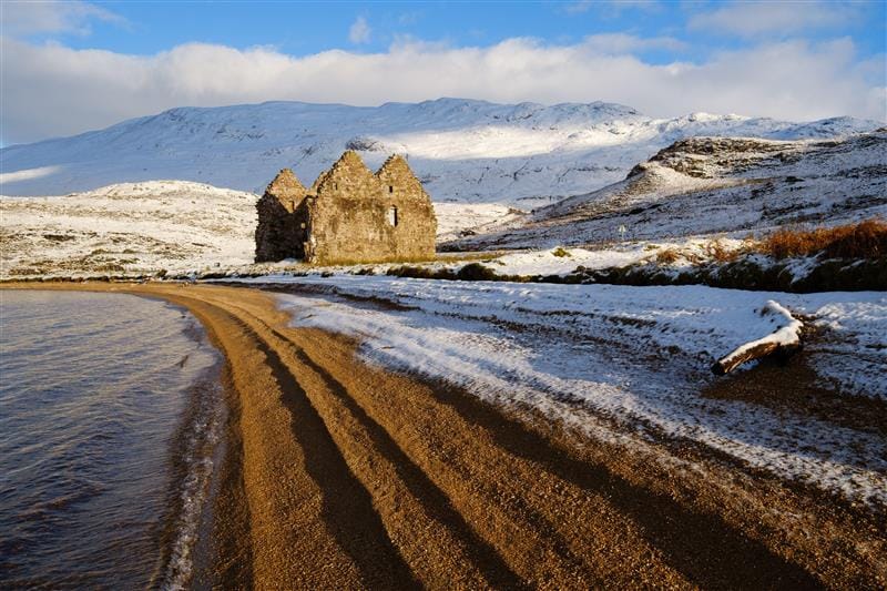 The ruined Calda House sits near the shoreline with snow covering the landscape.