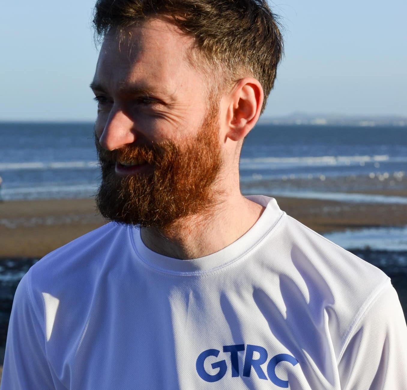 Craig Hannigan smiles with a beach in the background.