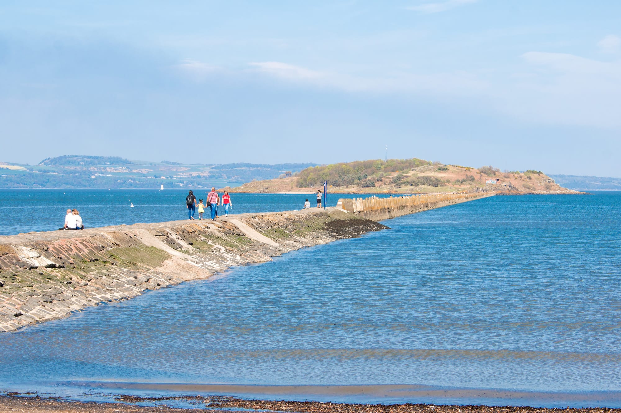 People walk the causeway to Cramond Island on a sunny day.