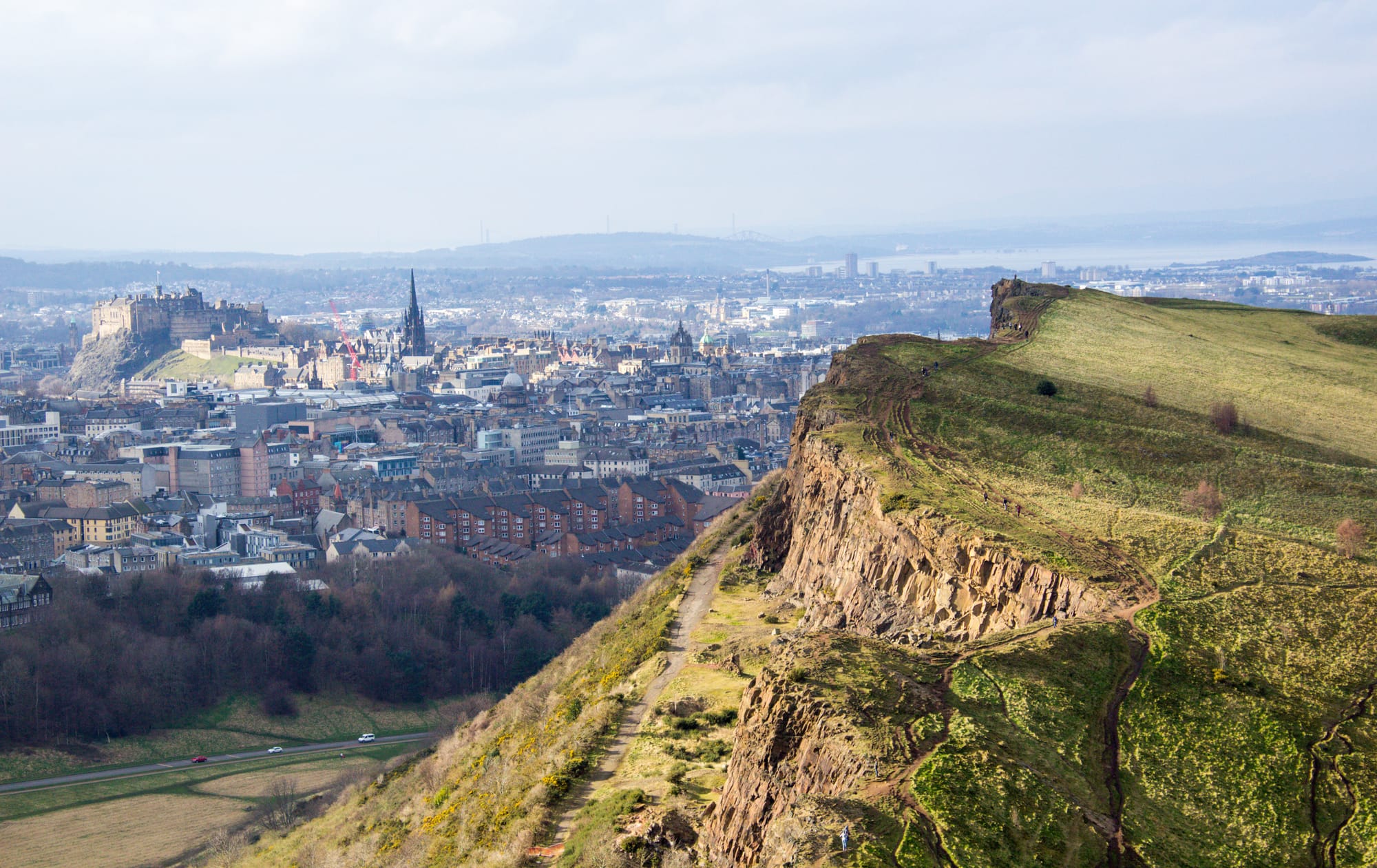 An aerial shot of Arthur's Seat with the city and the castle in the background.