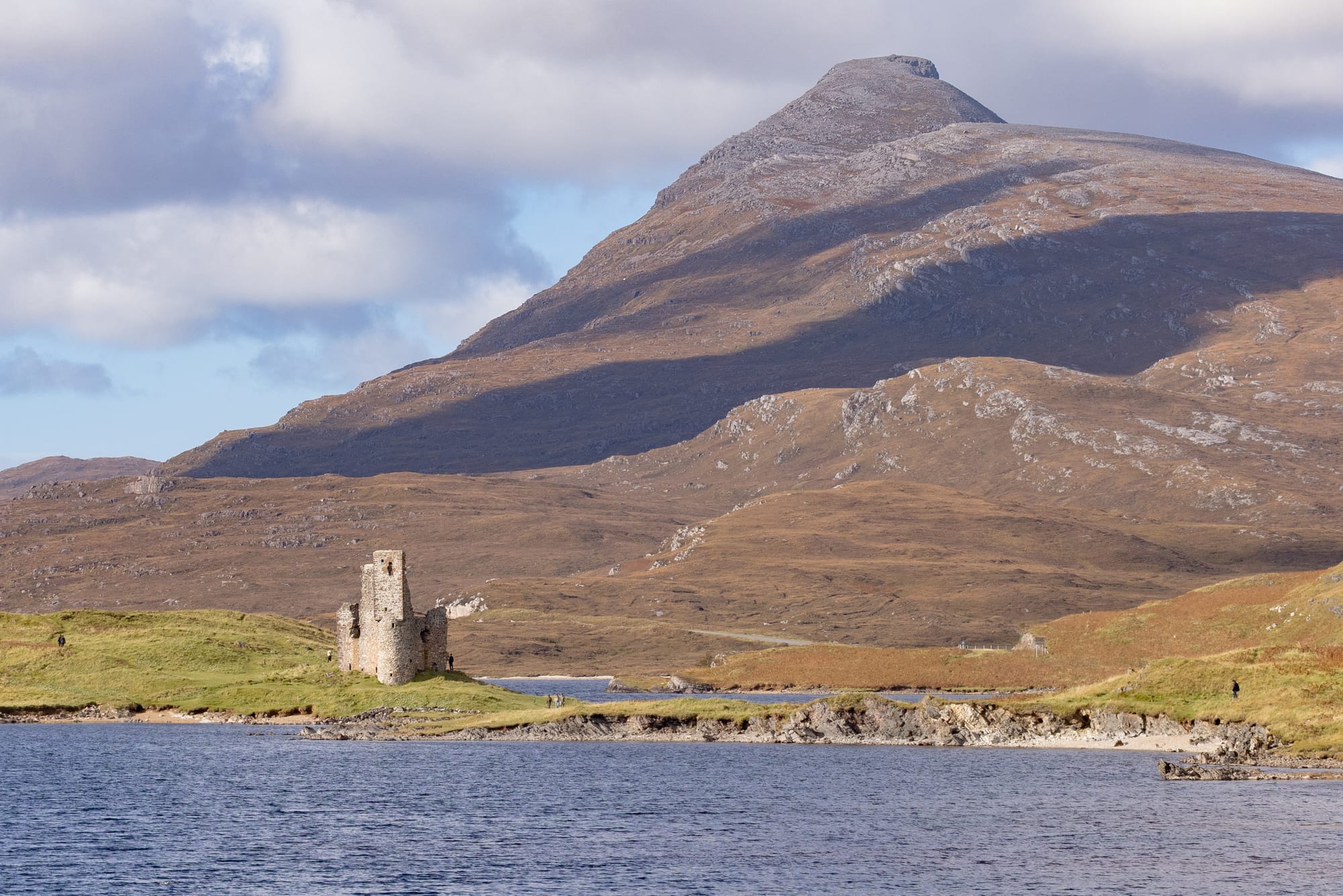 The ruin of Ardvreck Castle with a mountain behind it. There is water in the foreground.