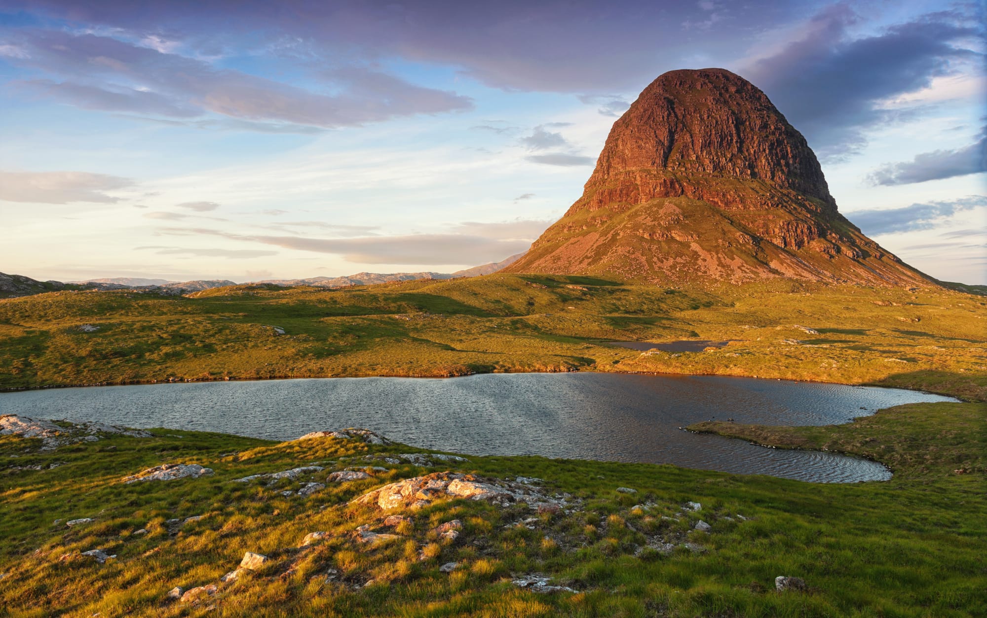 The rounded dome of Suilven is in the background of the image taken at sunset.