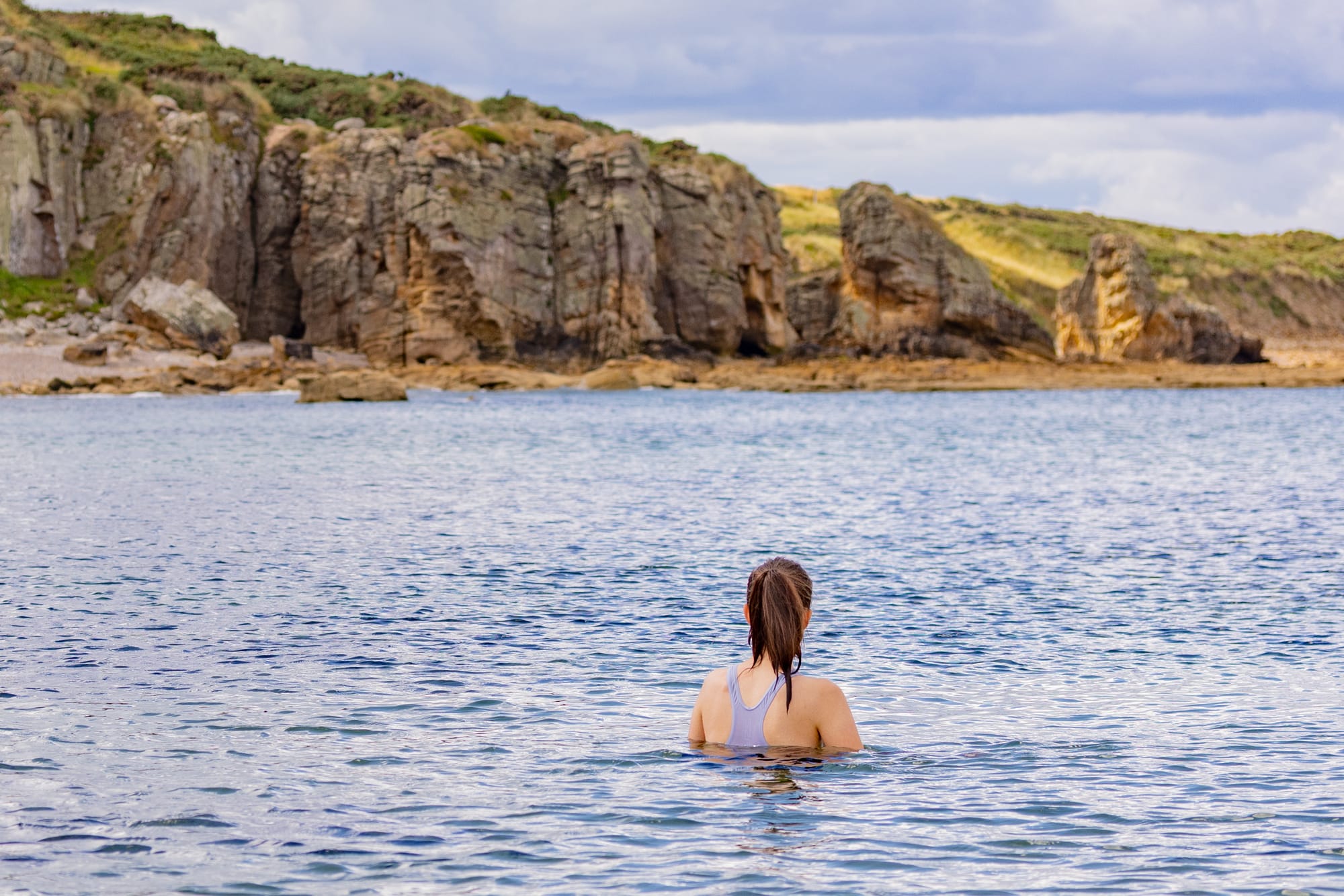A swimmer in blue water with cliffs in the background.