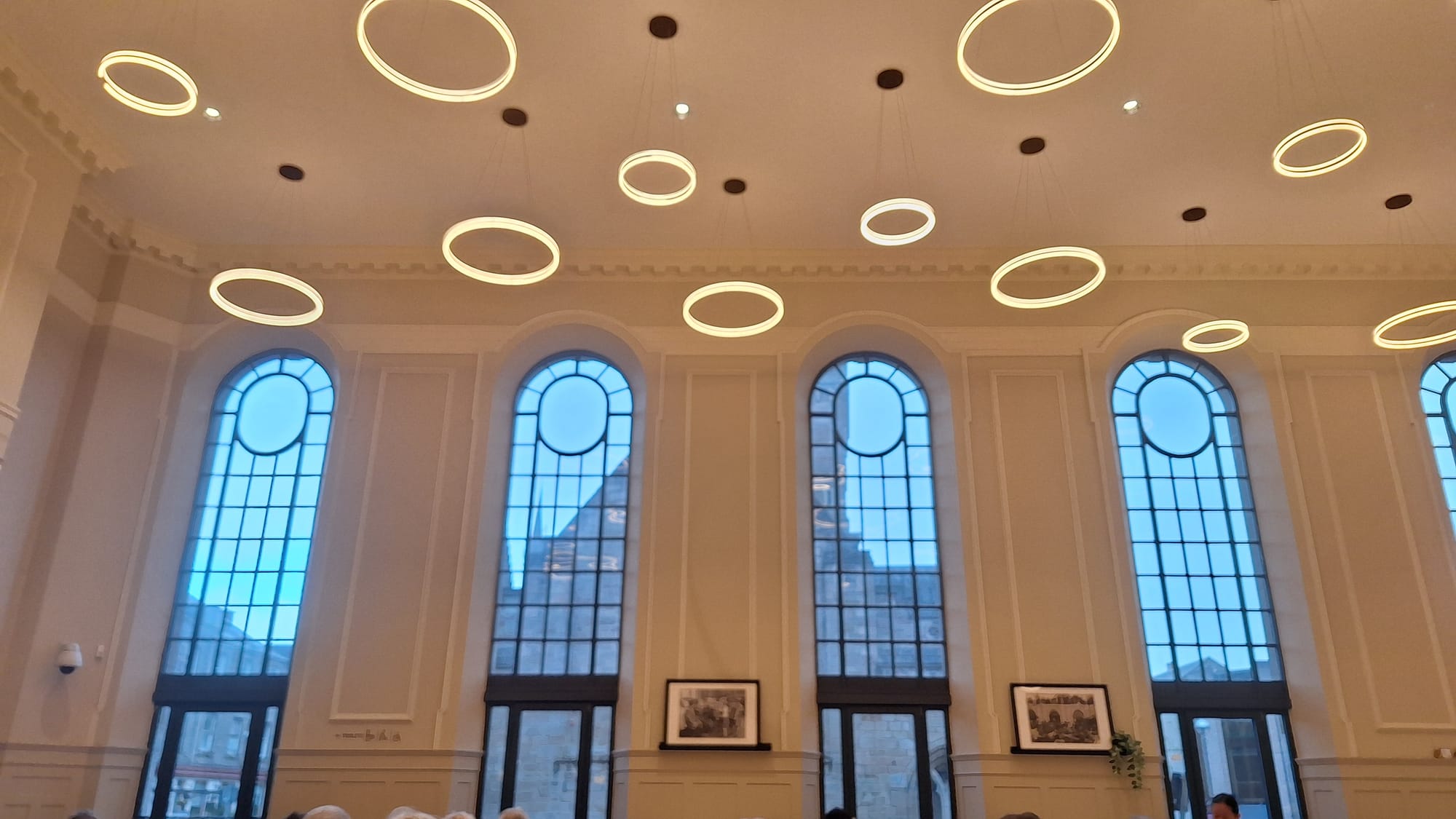A series of tall windows light up Perth Museum's Stone café. The ceiling is covered with circular lights.