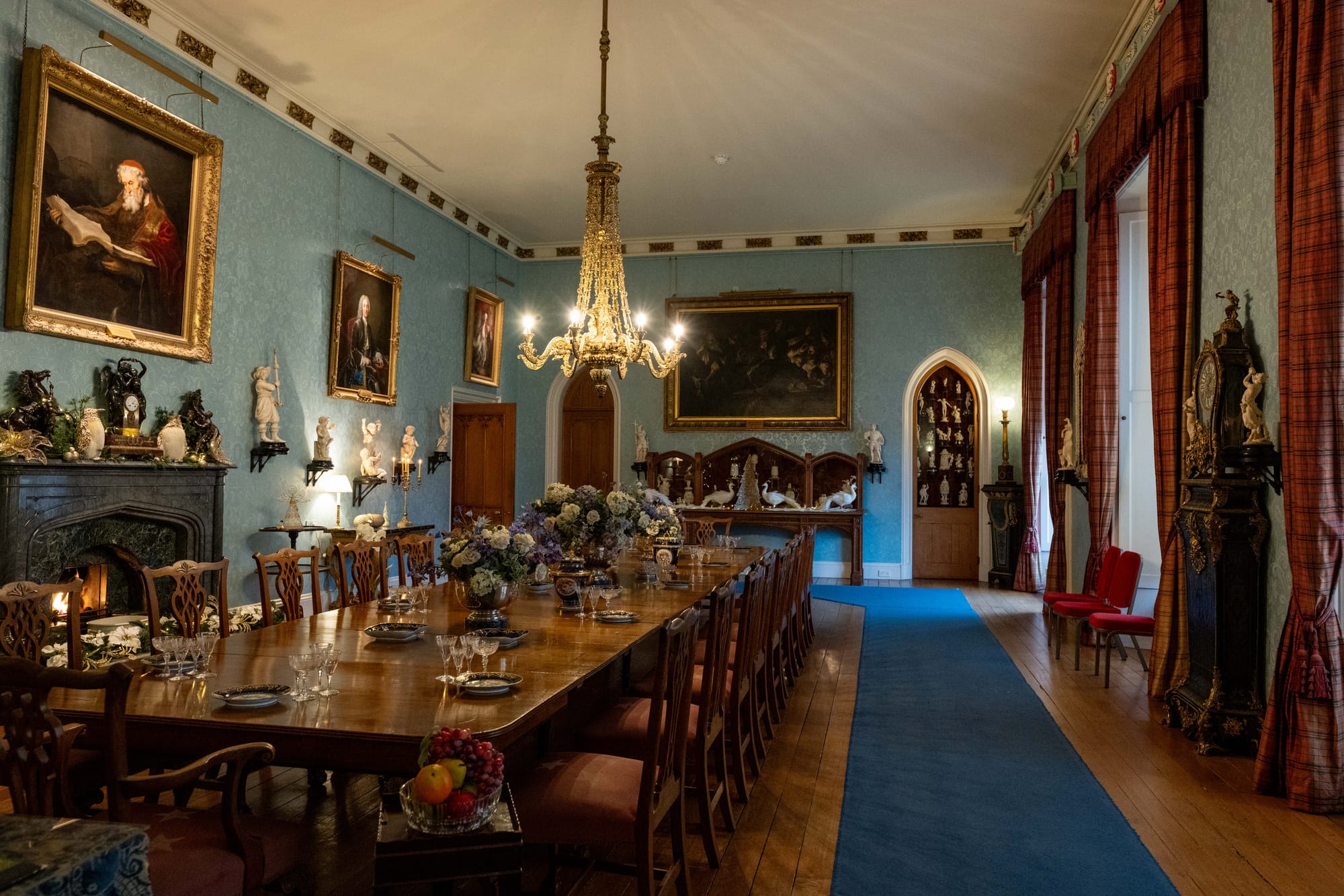A grand dining room with shiny wooden furniture, pale blue walls covered in artwork and a darker blue runner on the floor.