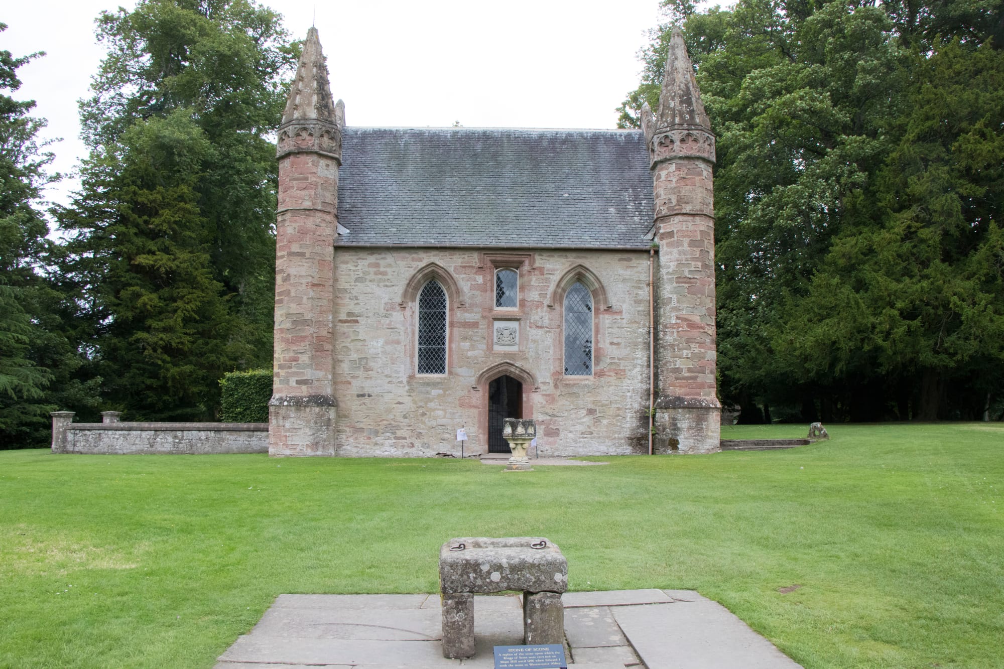 A replica of the Stone of Destiny at Moot Hill in the foreground. There is a chapel in the background.