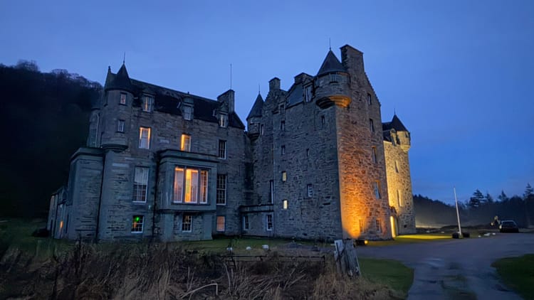 Castle Menzies at night. The castle is lit by golden lamps from within, and from spot lights on the lawn. 