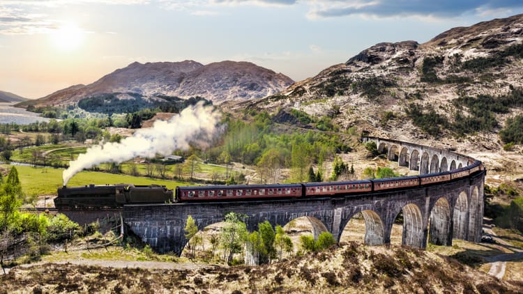 An aerial view of a steam train crossing the Glenfinnan Viaduct.
