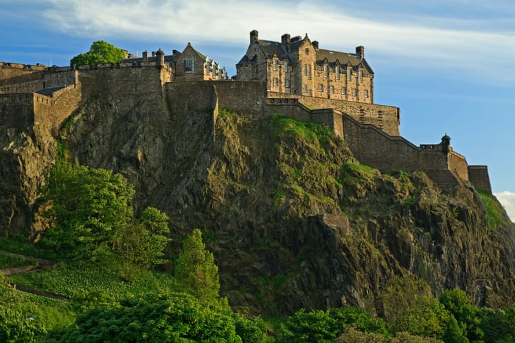 Edinburgh Castle sits atop Castle Rock with greenery growing on the slopes and a park below.