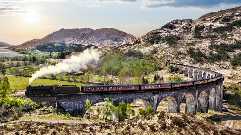 An aerial view of a steam train crossing the Glenfinnan Viaduct.
