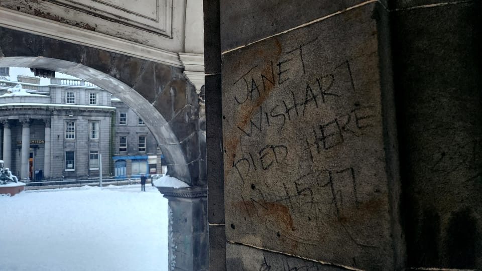 Graffiti written beneath a monument in Aberdeen that says 'Jane Wishart Died Here In 1597'.