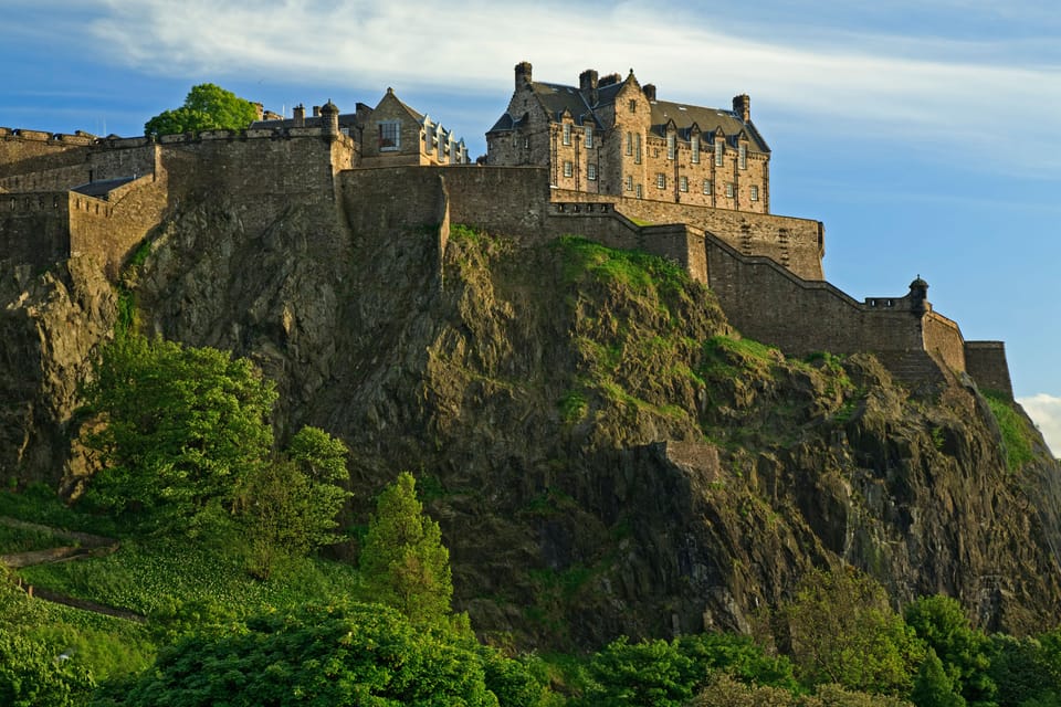 Edinburgh Castle sits atop Castle Rock with greenery growing on the slopes and a park below.