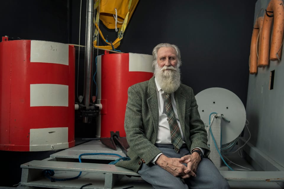 Adrian Shine, a man with white hair and a long white beard, in a tweed jacket. He is next to underwater equipment.